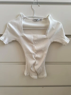 Vit ribbad topp från NA-KD - Ribbad topp från NA-KD med fyrkantig ringning och korta ärmar. Toppen har en snygg rynkning framtill som ger en cool detalj och sitter figurnära. Perfekt att styla med jeans eller kjol för en clean look 🫶🏻☀️