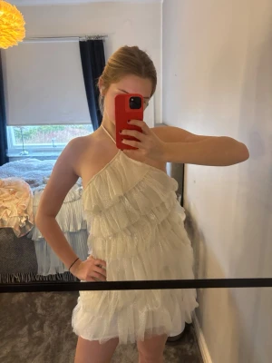 Vit glittrig  klänning - Supersöt vit kortklänning med glittriga detaljer och volanger. Lätt och luftig med flera lager volangtyg som ger en festlig känsla. Använd 1 gång endast och köpt från Cider.