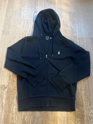 Marinblå hoodie från Polo Ralph Lauren - Snygg marinblå hoodie från Polo Ralph Lauren med dragkedja framtill och klassisk vit logga på bröstet. Hoodien har huva med dragsko och ribbade muddar vid ärmar och nederkant. Tillverkad i mjukt bomullsmaterial för skön känsla. Köpt för 2300 kr, pris kan även diskuteras😊