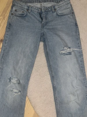 Ljusblå raka jeans med slitningar - Säljer ett par ljusblå jeans med raka ben och snygga slitningar på både lår och knä. Jeansen har klassisk femficksmodell och normal midja. Perfekta för en avslappnad och trendig look.
