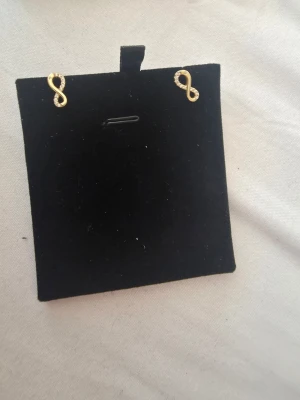 18 karat guld infinity örhängen med stenar - Snygga örhängen i form av infinity-tecken i 18 karat guld med små glittrande stenar på ena sidan av symbolen. Perfekta för dig som gillar stilrena men ändå iögonfallande accessoarer. Passar till många olika looks och är lätta att bära hela dagen. Köpt hos al hussien guld på Nørrebro I København 
