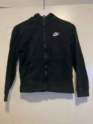 Svart Nike Tröja / Hoodie / Träningströja - Svart Nike tröja / hoodie med dragkedja och hög hals med luva. I bra använt skick. Har några små skavanker på insidan av dragkedjan (bild 7), ingenting som påverkar funktionen. Dragkedjan går att öppna och stänga som vanligt. Storlek M, liten i storleken. Passar mer som en S.