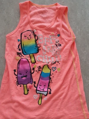 Linnetopp - Säljer ett färgglatt linne från Faded Glory med tryck av glada glassar i blått, gult och lila samt texten 'BFFs are so chill!'. Perfekt för dig som gillar lekfulla prints och somriga vibes.