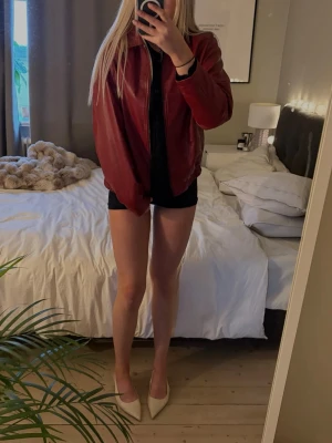 Vinröd skinnjacka  - Säljer en vinröd skinnjacka. Jackan har en rak passform, dragkedja framtill och ribbade muddar vid ärmslut och midja. 