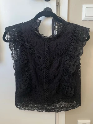 Svart spetsblus från only - Säljer en svart blus i spets från only i storlek xs.  Den har fina volangdetaljer längs ärmar och nederkant. Blusen är ärmlös och har hög hals med dragkedja i nacken. Passar riktigt bra när man vill känna sig extra snygg. Använd 1 gång. Nypris 500.