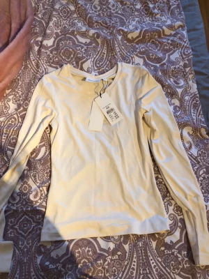 Kräm färgat långärmad topp Kappahl - Vit/ créme färgat  långärmad topp från Kappahl i mjuk bomull. Enkel och stilren design med rund halsringning och normal passform. Perfekt att matcha med jeans eller kjol för en clean look.