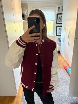 Vinröd och vit bomberjacka college - Snygg bomberjacka i klassisk college-stil med vinröd kropp och vita ärmar. 