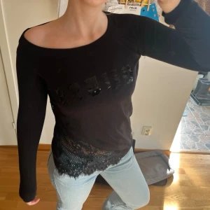 Svart topp med spets  - svart topp med lång ärm, paljet,text framtill och bred spetskant nedtill. Har krympt i tvätten så passa xs-s