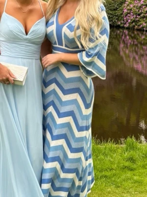 Blåvit stickad långklänning  - Säljer en långklänning från Indiska i stickat material med blå och vita breda zigzag-ränder. Klänningen har v-ringning, trekvartsärmar och markerad midja. Perfekt för dig som vill ha en unik och färgglad look. Formar kroppen fint och framhäver former. Når ner till anklarna på mig som är ca 170 cm lång. Enbart använd en gång. XS men mer som S. 