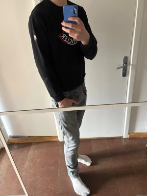 Svart Moncler sweatshirt - Säljer en svart sweatshirt från Moncler med stort broderat logotyptryck i vitt, rött och blått på bröstet. Tröjan har rund halsringning, långa ärmar och ribbade muddar vid ärmslut och nederkant. Klassisk och stilren design med Moncler-märke på ärmen och bröstet. Möjlighet finns att scanna NFC-tag