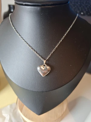 Silverfärgat halsband med hjärthänge - Snyggt halsband i silverfärg med ett blankt hjärthänge. Kedjan är tunn och stilren, och hjärtat har en mjukt rundad form. Perfekt accessoar för att lyfta vilken outfit som helst. Märke och material är ej angivet.