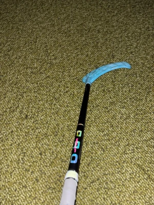 Innebandyklubba med blått blad - Säljer en innebandyklubba från PRO med svart skaft och ett ljusblått plastblad. Skaftet har färgglada bokstäver och ett vitt grepp längst ner. Perfekt för dig som vill spela innebandy eller bara ha kul med kompisarna.
