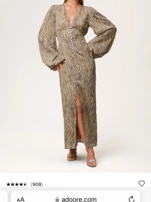 Zebramönstrad långklänning från Adoore - Snygg långklänning från Adoore med zebramönster i beige och grå toner.( ganska liten i storleken)  Klänningen har v-ringning, knappar framtill, långärmade puffärmar och en slits framtill. Perfekt för dig som vill sticka ut med en trendig look. 💛💛💛