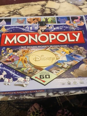 Monopol Disney Edition brädspel - Säljer ett Monopol Disney Edition brädspel med klassiska Disney-karaktärer och motiv på spelplanen. Lådan är blå och dekorerad med figurer som Bambi, Alice i Underlandet och 101 dalmatiner. Innehåller 6 exklusiva spelpjäser och färgglada spelkort.