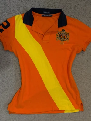 Ralph Lauren vintage pikétröja S - Vintage Ralph Lauren pikétröja i orange med gul diagonal rand och broderad logga framtill samt patch på ärmen. Små fläckar se bilderna. Annars mycket fint skick💕  Längd: 59cm Bred midja: 35cm