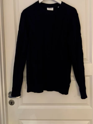 Mörkblå kabelstickad tröja Lindbergh - Mörkblå kabelstickad tröja från Lindbergh med rund halsringning och ribbade muddar. Tröjan har ett klassiskt flätmönster. Materialet är mjukt och bekvämt.