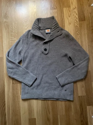 Beige stickad ull Hugo boss tröja  - Säljer en biege stickad tröja med ribbad hög krage och två knappar framtill. Tröjan har långa ärmar och är tillverkad i ett mjukt, värmande material. Perfekt för kyliga dagar och enkel att matcha med jeans eller chinos.