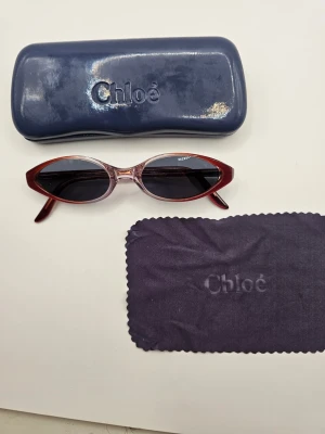 Röda cat eye solglasögon från Chloé - Snygga cat eye solglasögon från Chloé med röda bågar och mörka linser. Glasögonen har en cool retroform och kommer med originalfodral och putsduk. Perfekta för dig som vill sticka ut med en trendig accessoar. Vet inte om de är äkta eller inte 