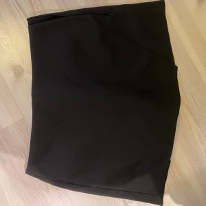 Svart kortkjol med shorts - Snygg svart kortkjol med omlottdesign och diskreta fickdetaljer bak. Kjolen har en stilren look och passar perfekt till många olika outfits. Tillverkad i ett mjukt och följsamt material som ger en bekväm passform.