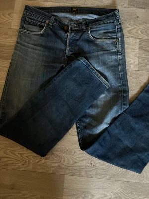 Blå raka jeans från Lee - Snygga blå jeans från Lee med raka ben och klassisk femficksdesign. Jeansen har en lätt tvättad look med slitningar på låren och kontrastsömmar. Perfekta för en avslappnad stil och tillverkade i bomullsdenim. Hör av er om ni har frågor eller vill ha fler bilder!