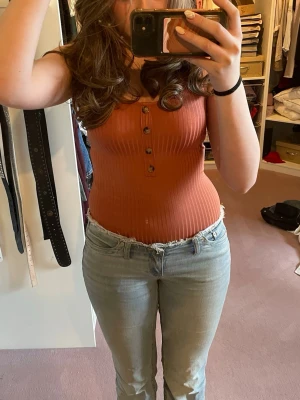 Rostfärgad ribbad body med knappar - Snygg rostfärgad ribbad linnebody med knappar framtill. Perfekt att styla med jeans eller kjol. Från hm i storlek xs. Som ny endast använd fåtal gånger. Hör av dig vid frågor/intresse 💞