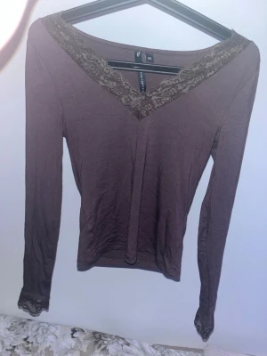 Brun långärmad topp med spets - Mysig brun långärmad topp från lager157 med v-ringning dekorerad med spetsdetaljer. Toppen har även spets vid ärmsluten och är i en mjuk, stretchig bomullsblandning. Perfekt för dig som gillar en enkel men ändå söt stil. 