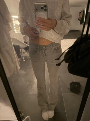 Grå bootcut jeans med låg midja - Säljer ett par gråa bootcut jeans med låg midja och klassiska fem fickor. Jeansen har en snygg tvätt och sitter tajt över höfterna för en trendig look. Perfekta för dig som gillar en avslappnad men ändå stilren stil.