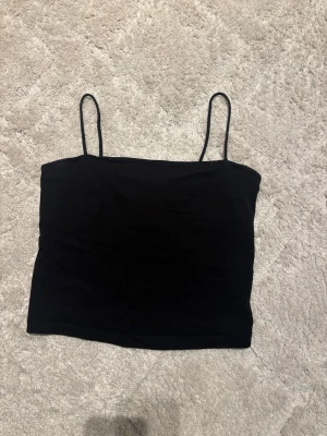 Svart linnetopp från Gina Tricot - Säljer en svart linnetopp från Gina Tricot med tunna axelband. Toppen är enkel och stilren, perfekt att matcha med olika outfits. Materialet är mjukt och stretchigt, vilket gör den bekväm att bära. Finns även en extra tygbit på insidan över bysten.