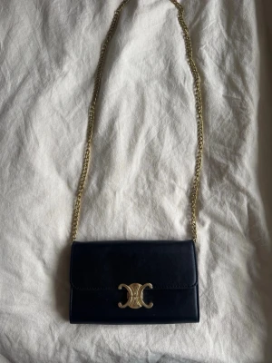 Svart väska - Snygg svart handväska  med guldfärgad kedjerem. Väskan är i slät läder och har en stilren, rektangulär form som passar perfekt till en trendig look. Guldmärket har tappat lite färg (se bild) men inget märkvärdigt. Har använts ett fåtal gånger. 