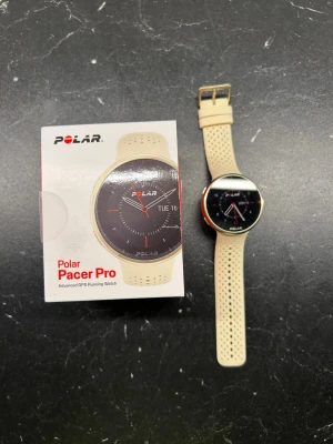 Polar Pacer Pro beige smartklocka - Polar Pacer Pro smartklocka med beige silikonarmband och rund urtavla. Klockan har GPS, pulsmätare och sportfunktioner. Perfekt för löpning och träning. Stilren design med perforerat armband för extra komfort. Levereras med originalförpackning. Inköpt januari 2026.