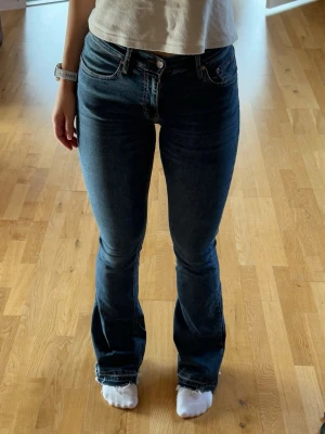 Mörkblå bootcut jeans - Snygga mörkblå bootcut jeans med klassisk femficksdesign och råa kanter vid bensluten. Jeansen har hög midja och sitter tight över låren för en schysst siluett. Dessvärre har den ett hål vid högra bakfickan