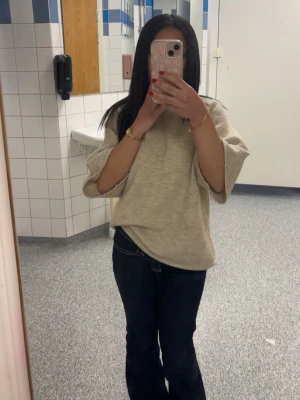 Beige stickad tröja med vida ärmar - Säljer en beige stickad tröja med trekvarts vida ärmar och avslappnad passform. Tröjan har en enkel design utan synliga mönster och är perfekt för en chill och stilren look. Passar bra till jeans eller kjol.