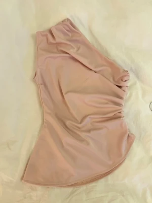 Ljusrosa bikiniöverdel one shoulder - Trendig ljusrosa bikiniöverdel i one shoulder-modell med lätt rynkade detaljer på sidan. Perfekt för sommarens strandhäng och poolpartyn. Tillverkad i mjukt syntetmaterial som sitter bekvämt mot huden.