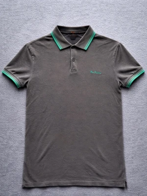 Ben Sherman Polo Shirt – British Mod / Terrace Style – S - Klassisk Ben Sherman polo shirt i mörkgrå ton med gröna kontrastdetaljer i kragen och ärmarna.  En tidlös piké som passar perfekt för British mod / casual style.  Detaljer: • Ben Sherman • Storlek S • Mycket bra skick • Pikéstruktur i tyget • Kontrastdetaljer i grönt • Klassisk polokrage med knappar  Perfekt till jeans, chinos eller shorts för en clean British casual look.  📦 Skickas snabbt 💬 Hör gärna av dig vid frågor