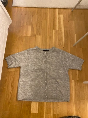 Grå kofta med pärlknappar - Mysig grå kofta med korta ärmar och pärlknappar framtill. 