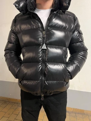 Moncler Jacka - Svart glansig vinterjacka från Moncler. Jackan är i storlek S och nyskick, inga tecken på använd. Väldigt bekväm och varm samt väldigt snygg, rekommenderar starkt. Hör av dig vid intresse/funderingar. PRIS KAN DISKUTERAS!