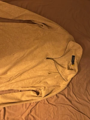 Beige halvzip-tröja från Polo Ralph Lauren - Snygg beige långärmad tröja från Polo Ralph Lauren med halvzip och diskret broderad logga på bröstet. Tillverkad i mjukt material som passar perfekt till lager-på-lager. Enkel och stilren design som funkar till det mesta.