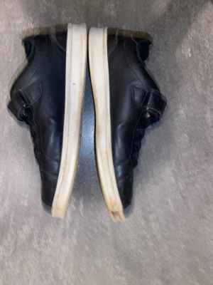 Svarta sneakers med kardborreband - Svarta sneakers med vita sulor och kardborreband. Skorna har klassisk låg profil, svarta skosnören och är tillverkade i syntetmaterial. Perfekta för en avslappnad och sportig stil.