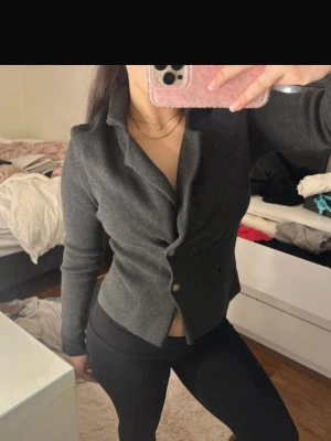 Mörkgrå figursydd kavaj - Snygg mörkgrå kavaj med figurnära passform och två knappar framtill. Kavajen har klassisk krage och är tillverkad i ett mjukt, stretchigt material som ger en bekväm känsla. Perfekt för dig som vill ha en stilren och modern look.