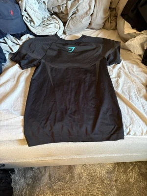 Svart t-shirt från Gymshark Onyx serien - Säljer en svart t-shirt från Gymshark med sportig design och meshdetaljer upptill. T-shirten har korta ärmar och är tillverkad i ett lätt och stretchigt material som passar perfekt till träning. Snygg passform och diskret logga i nacken.