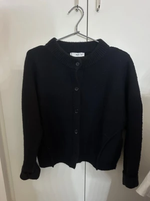 Mörkblå stickad kofta med knappar - En mörkblå stickad kofta med rund halsringning och ribbade muddar. Koftan har knäppning framtill med fyra knappar och en enkel, klassisk design som passar till det mesta. Perfekt för lager på lager och enkel att matcha. Från mango i storlek M. Knappt andvänd endast runt tre gånger. Den är liten i storlekarna så passar folk med s och xs också