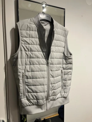 Ljusgrå dunväst från Autograph -  Ljusgrå dunväst från Autograph med quiltad design och två dragkedjeförsedda fickor. Västen har ribbade muddar vid krage och nederkant. Framsidan är dunförsedd, baksidan är av bomull. Använd <5 gånger! Hör av er vid frågor!!