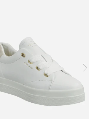 Vita sneakers från Gant - Stilrena vita sneakers från Gant med lågt skaft och guldfärgade detaljer vid snörningen. Skorna har breda vita skosnören och är tillverkade i slätt läder. Perfekta för en clean och klassisk look.