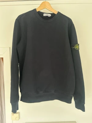 Mörkblå sweatshirt från Stone Island - Klassisk mörkblå sweatshirt från Stone Island med rund halsringning och ikonisk logopatch på vänster ärm. Tröjan har ribbade muddar vid ärmslut och nederkant, perfekt för en clean och stilren look. Stl XL gott skick endast använd ett fåtal ggr och handtvättad i maskin