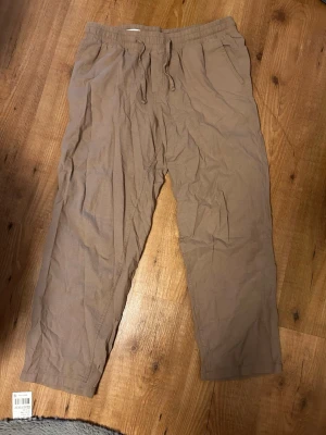 Beiga linnebyxor med dragsko - Säljer ett par beiga linnebyxor med avslappnad passform och resår i midjan samt dragsko. Byxorna har sidofickor och är tillverkade i ett lätt och luftigt linnematerial, perfekta för en chill och stilren look.