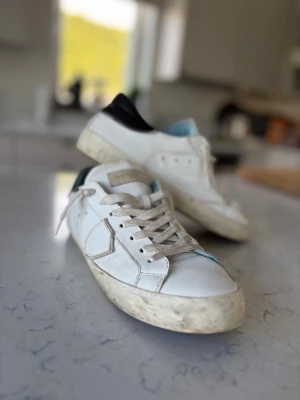 Philippe model, vita sneakers med svart häl, slitningar - Snygga sneakers från Philippe Model med naturliga slitningar och svart detalj på hälen. Skorna har klassisk låg profil, vita snören och diskreta sömmar. Läder. Sparsamt använda. Villig att diskutera pris vid snabb affär. 