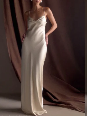 Champagnefärgad långklänning i satin - Elegant långklänning i champagnefärgad satin med tunna axelband och smickrande siluett. Klänningen har en mjukt draperad byst och en minimalistisk design som ger en lyxig känsla. Perfekt till bal eller andra festligheter. Klänningen är endast prövad och har alla lappar kvar. Postar fort!