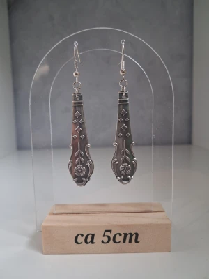 Unika örhängen återbruk handgjorda  - Säljer ett par handgjorda örhängen skapade av 2st bestick gjorda i nysilver. Är ca 5 cm långa. De har en vintageinspirerad design med ingraverade mönster och blommor. Perfekta för dig som gillar detaljerade accessoarer med retrovibbar. Öronkroken är nickelsäker och aldrig använda.