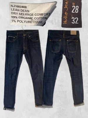 Nudie Jeans Lean Dean Dry Selvedge - Säljer ett par mörkblå Lean Dean jeans från Nudie Jeans med selvedge och slim fit. Jeansen är tillverkade av 99% ekologisk bomull och 1% polyuretan, vilket ger en bekväm stretch. Klassisk femficksdesign och snygga kontrastsömmar.