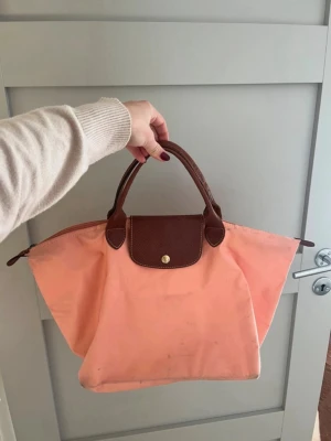 Longchamp väska - Jättefin äkta longchamp väska Le pilage modell Bra skick, men lite smutsig botten (se bild)    Longchamp, Le Pliage, rosa väska, ljusrosa, peach, peachfärgad, totebag, tote bag, handväska, shopper, nylonväska, vardagsväska, weekendbag, skolväska, märkesväska, designer, minimalistisk, clean girl, preppy, aesthetic, vintage, klassisk, vikbar väska, sommarväska, pink bag, pastel pink, peach bag, nylon tote, handbag, shopper bag, everyday bag, travel bag, foldable bag, designer bag, luxury tote, Fre